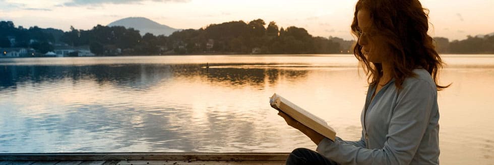 Individual reading book by lake.