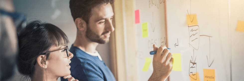 Three professionals stand in front of a whiteboard reviewing creative ideas.