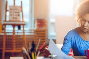 A learner sits at a desk and examines paperwork in front of an open laptop.