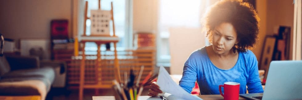 A learner sits at a desk and examines paperwork in front of an open laptop.