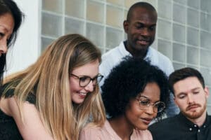 A group of coworkers sit at a table in the office, talking and smiling.